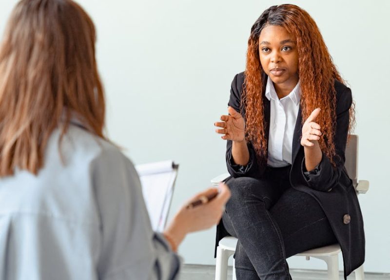 A mental health professional talking with a patient in a therapy session indoors.